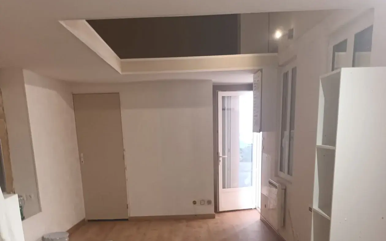 Appartement rénové : sol stratifié posé, murs repris et plafond décaissé à panneau sombre