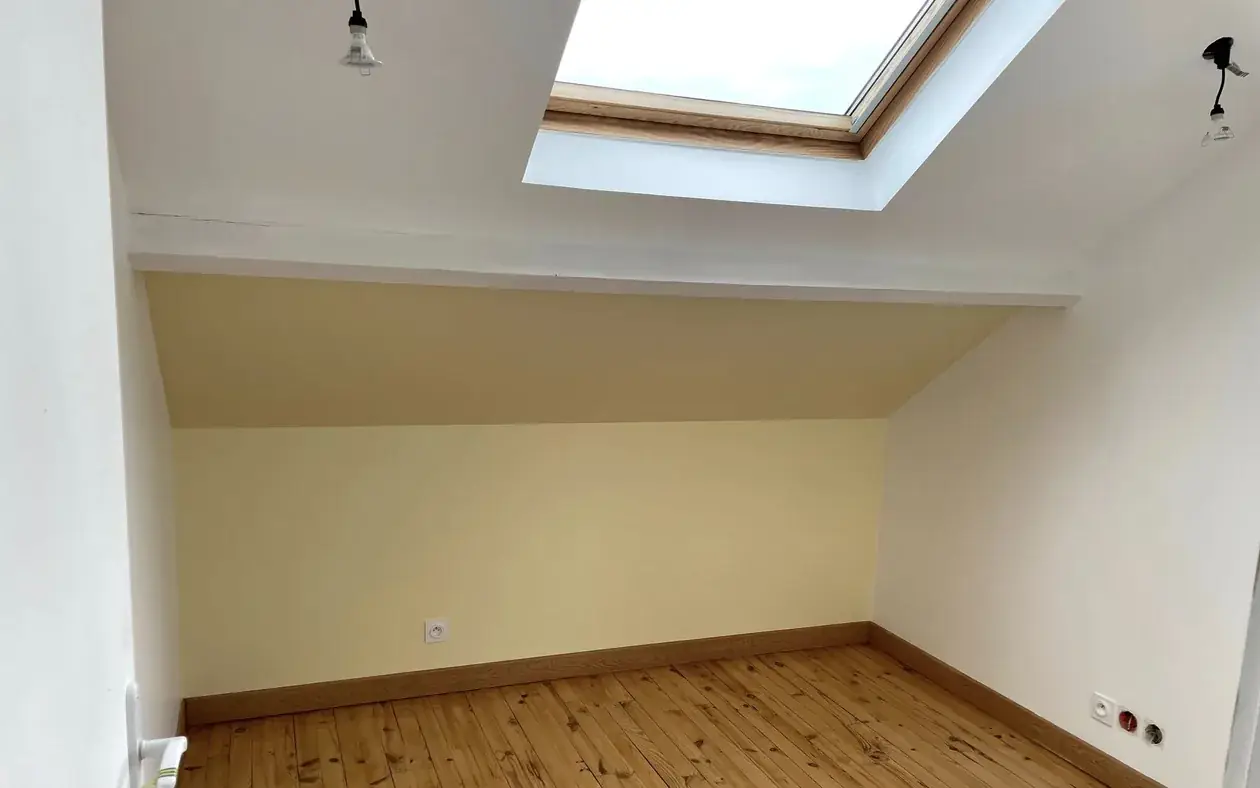 Chambre sous rampant termin&eacute;e : mur peint en jaune p&acirc;le, plafond blanc, fen&ecirc;tre de toit et parquet en pin d'origine conserv&eacute;