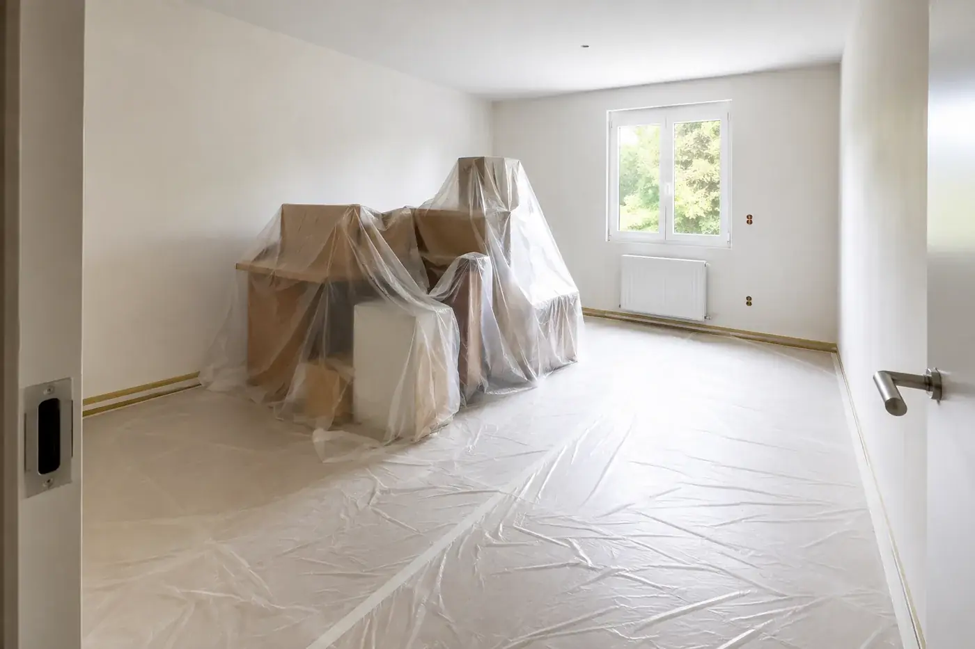 Pièce en cours de chantier : sol entièrement bâché, meubles regroupés et filmés sous plastique de protection