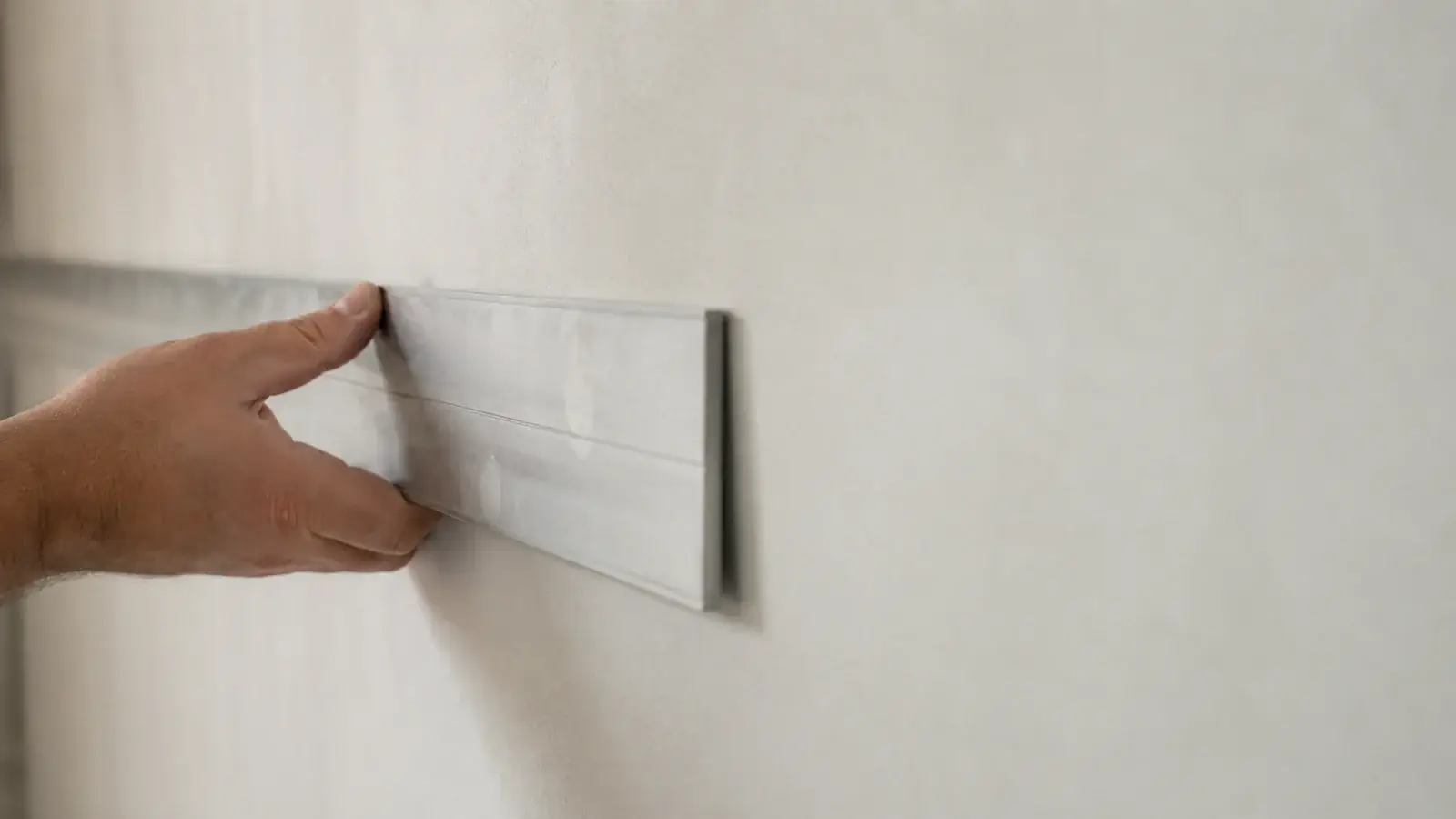 Règle métallique tenue à plat contre un mur fini, sans jour visible sous la règle