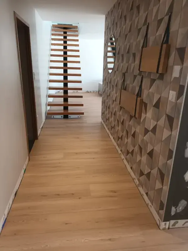 Couloir au sol à décor chêne clair posé dans le sens de la longueur, mur à motif géométrique et escalier à marches ouvertes