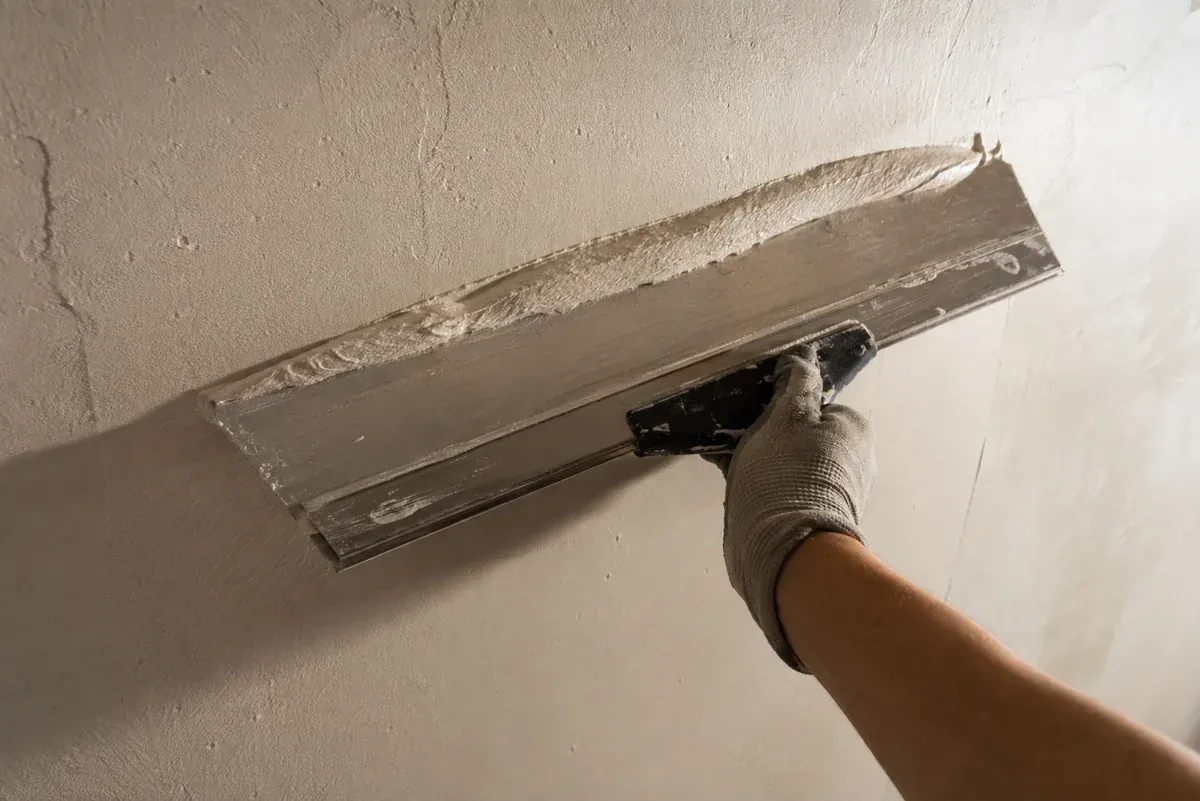 Couteau à enduire large tiré sur un mur : bourrelet d'enduit devant la lame, surface déjà lissée derrière