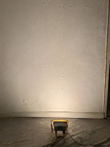 Mur éclairé en lumière rasante avant préparation : marques d'outil, reprises et microfissures visibles sur toute la surface