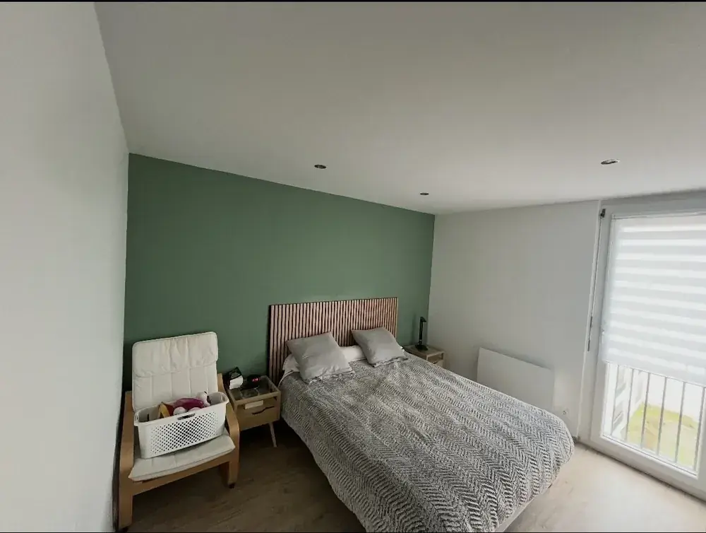 Chambre repeinte avec mur d'accent vert et tête de lit en tasseaux bois, réalisée par BATIMM RENOV