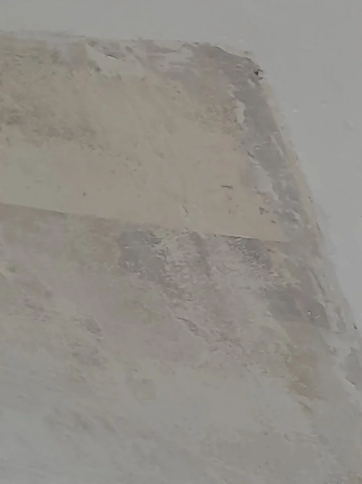 Gros plan d'un plafond ancien : une bande claire de reprise traverse une zone plus grise et grumeleuse, et la surface s'interrompt sur un bord droit