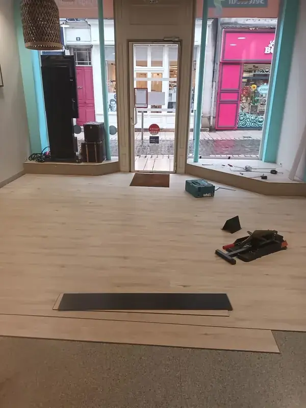 Pose de lames de sol vinyle en cours dans un local commercial, lames découpées et outils au sol