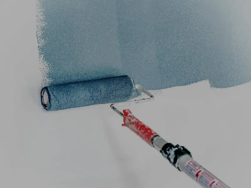 Rouleau appliquant une peinture bleu-gris sur un mur blanc