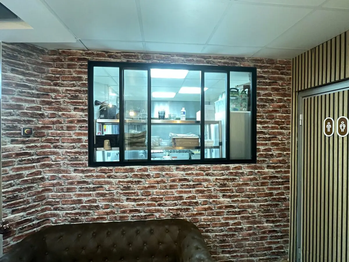 Verrière coulissante ouvrant sur la cuisine d'un restaurant, encastrée dans un mur en plaquettes de parement brique